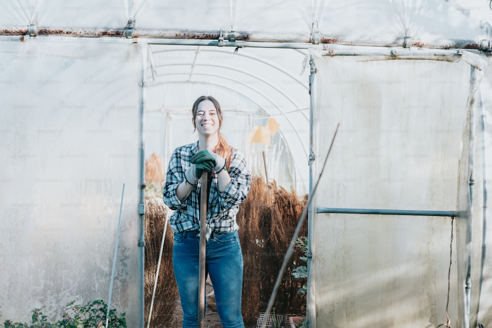 a woman standing in a greenhouse holding a shovel