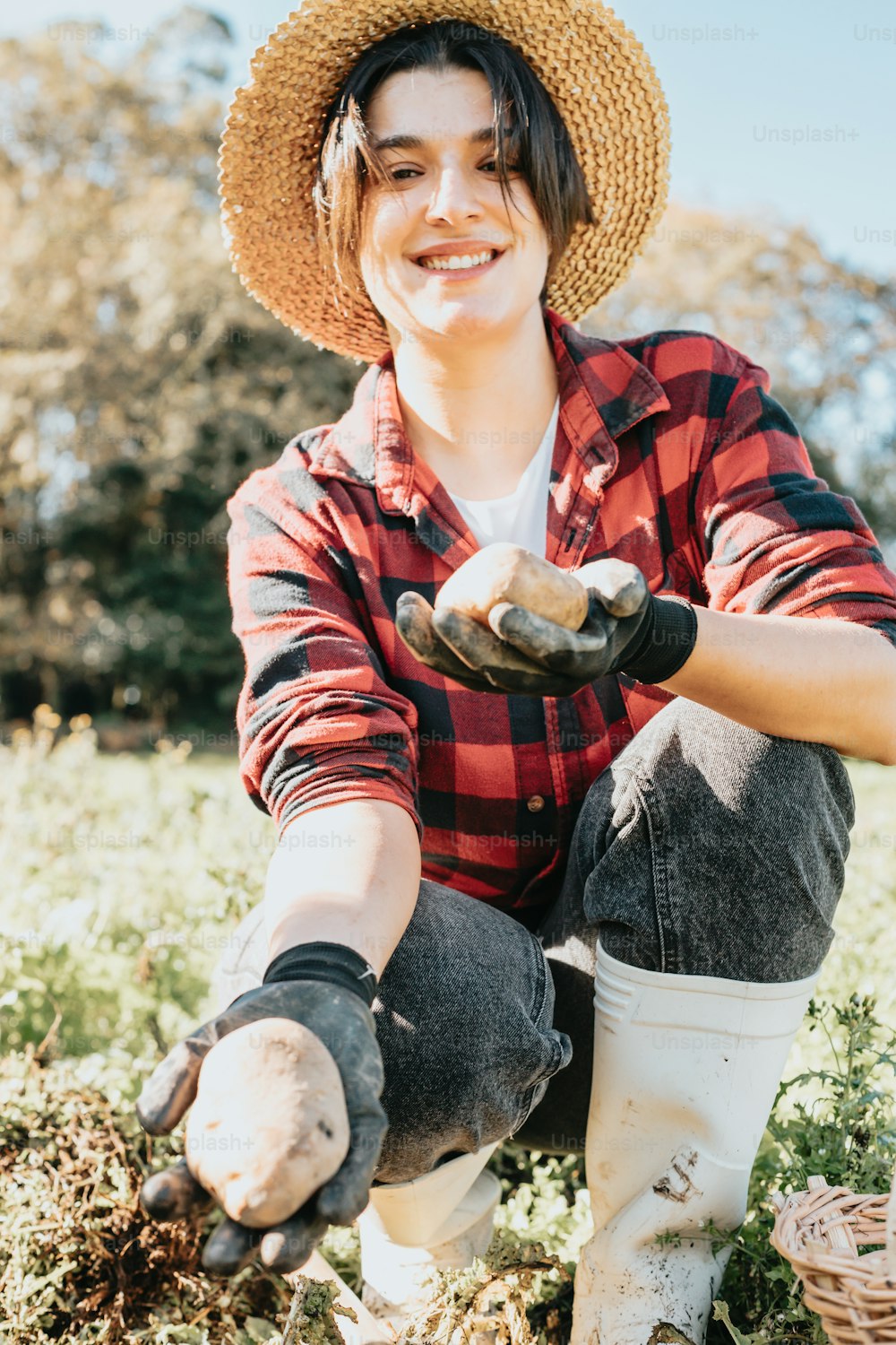 a man in a straw hat and plaid shirt crouching in a field