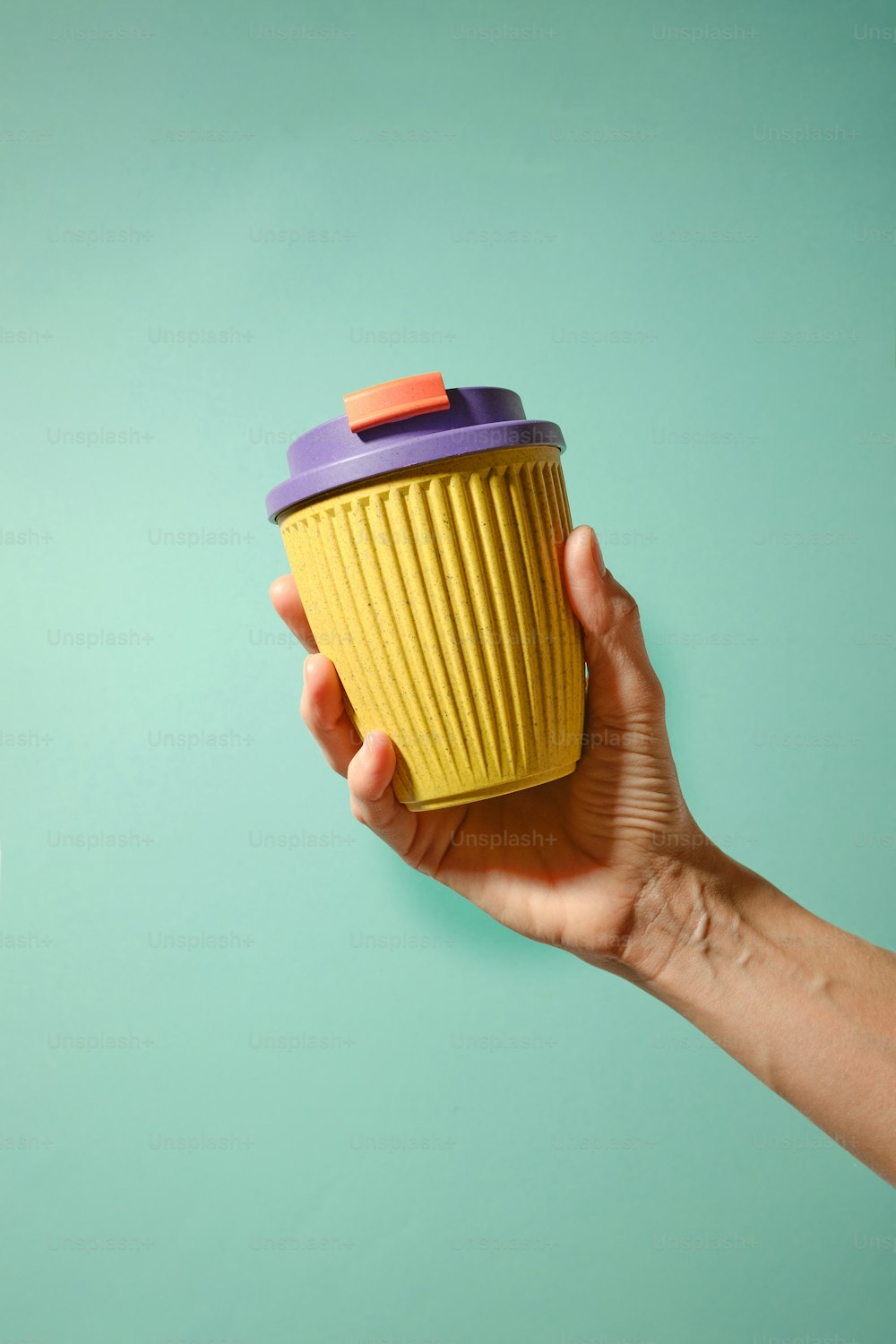una mano sosteniendo una taza amarilla con una tapa púrpura
