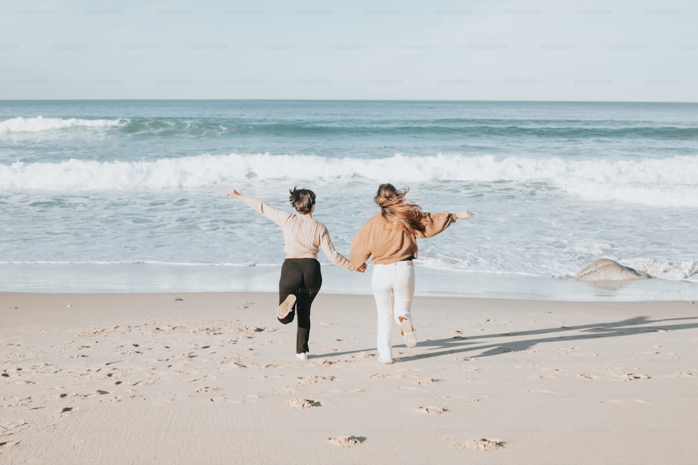 um casal de mulheres em pé em cima de uma praia de areia
