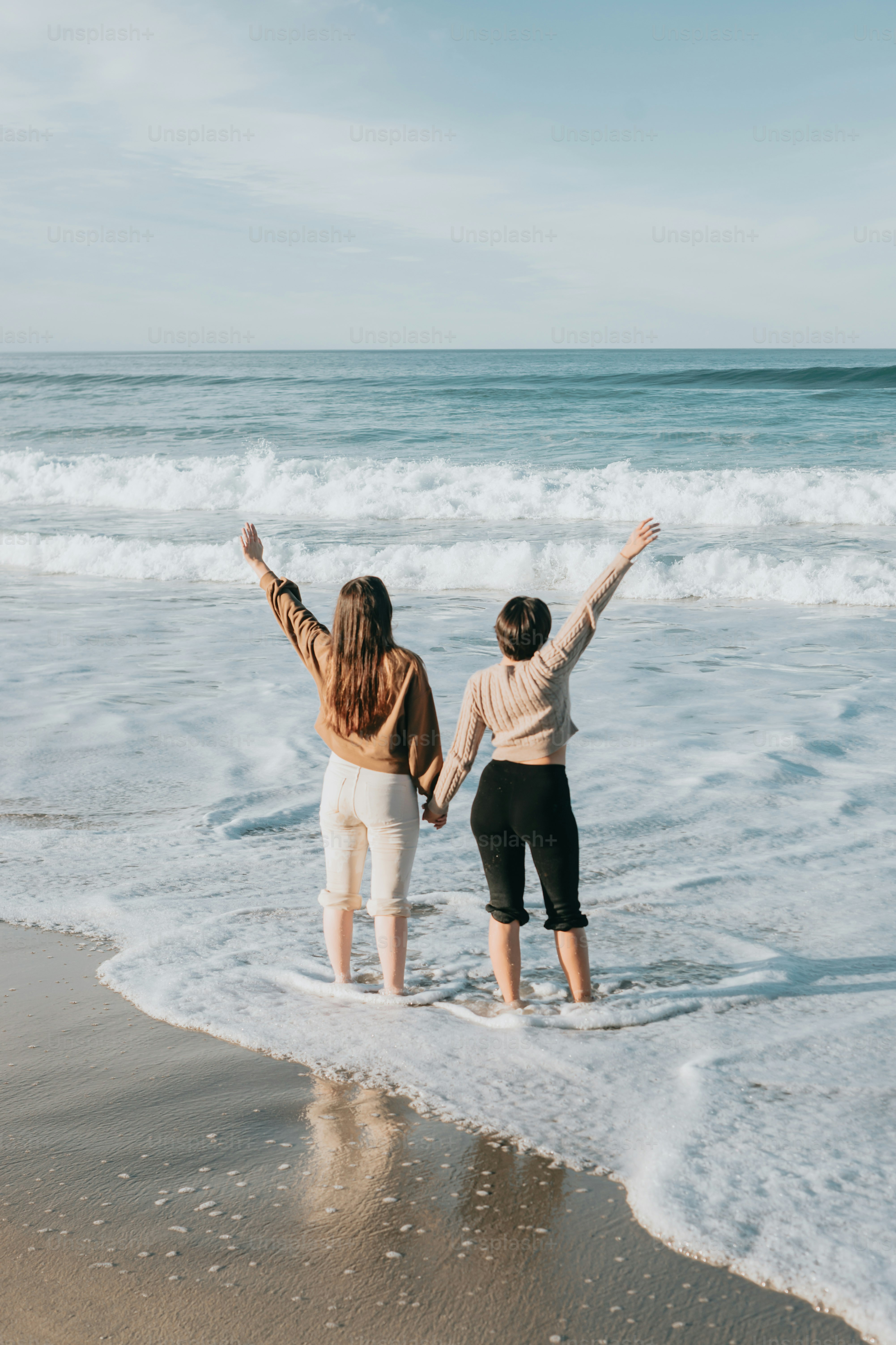 a couple of women standing on top of a sandy beach