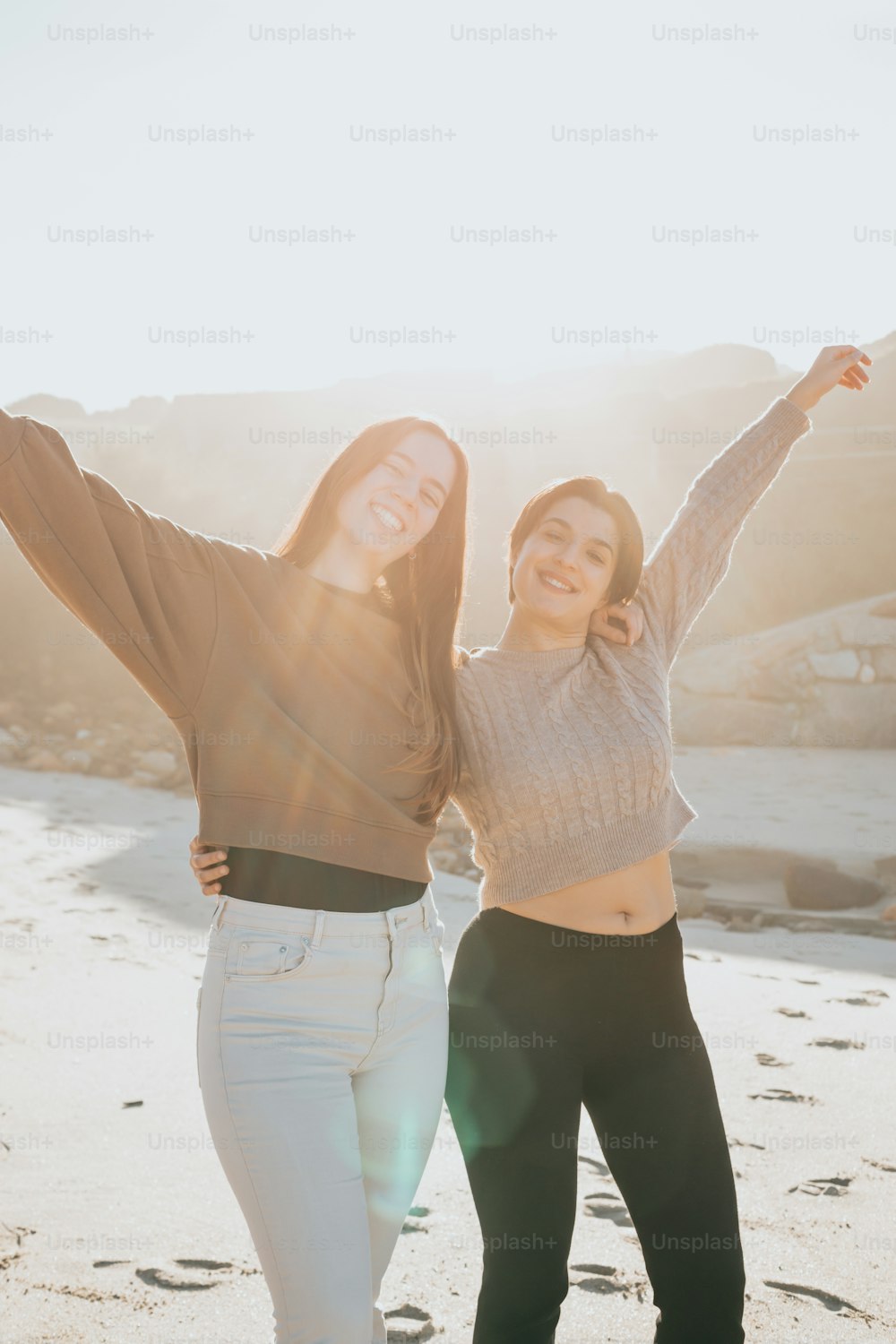 two women standing on a beach with their arms in the air