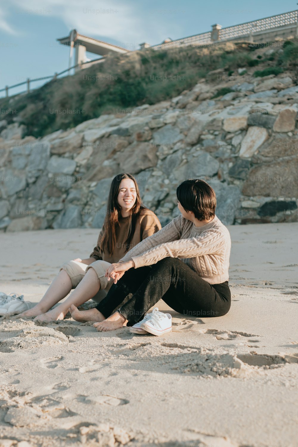 two women sitting on a beach next to each other