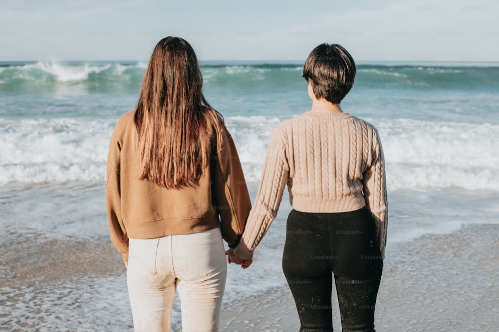Zwei Frauen, die Händchen haltend am Strand spazieren gehen