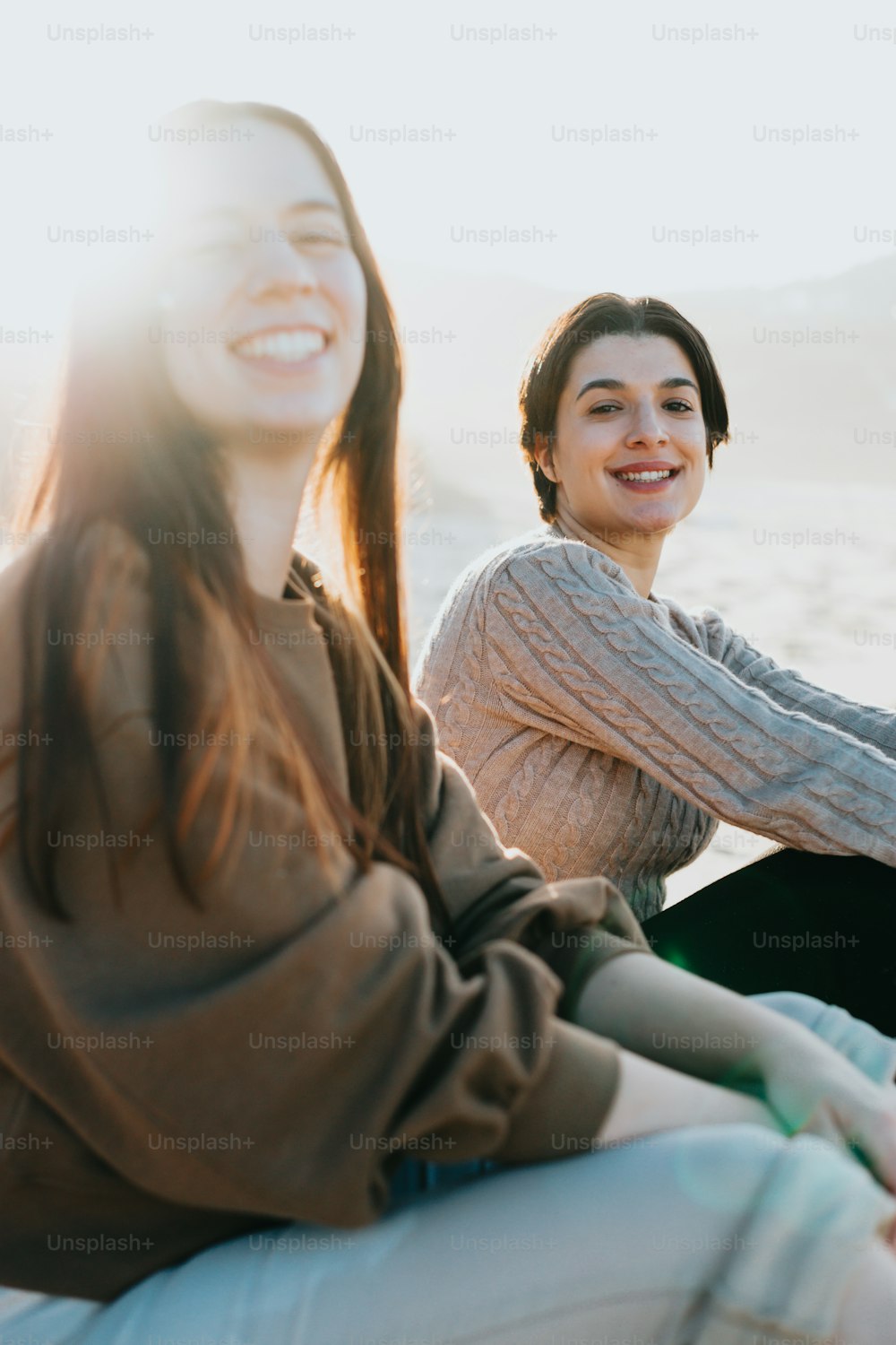 해변에 앉아 카메라를 향해 웃고 있는 두 여자