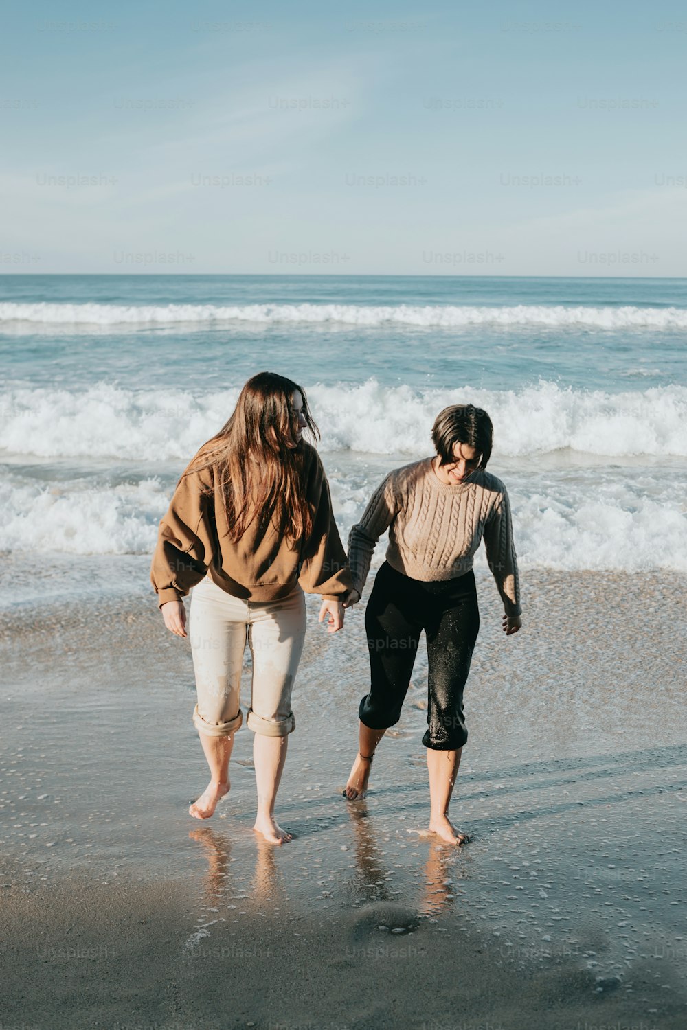 a couple of women walking along a beach next to the ocean