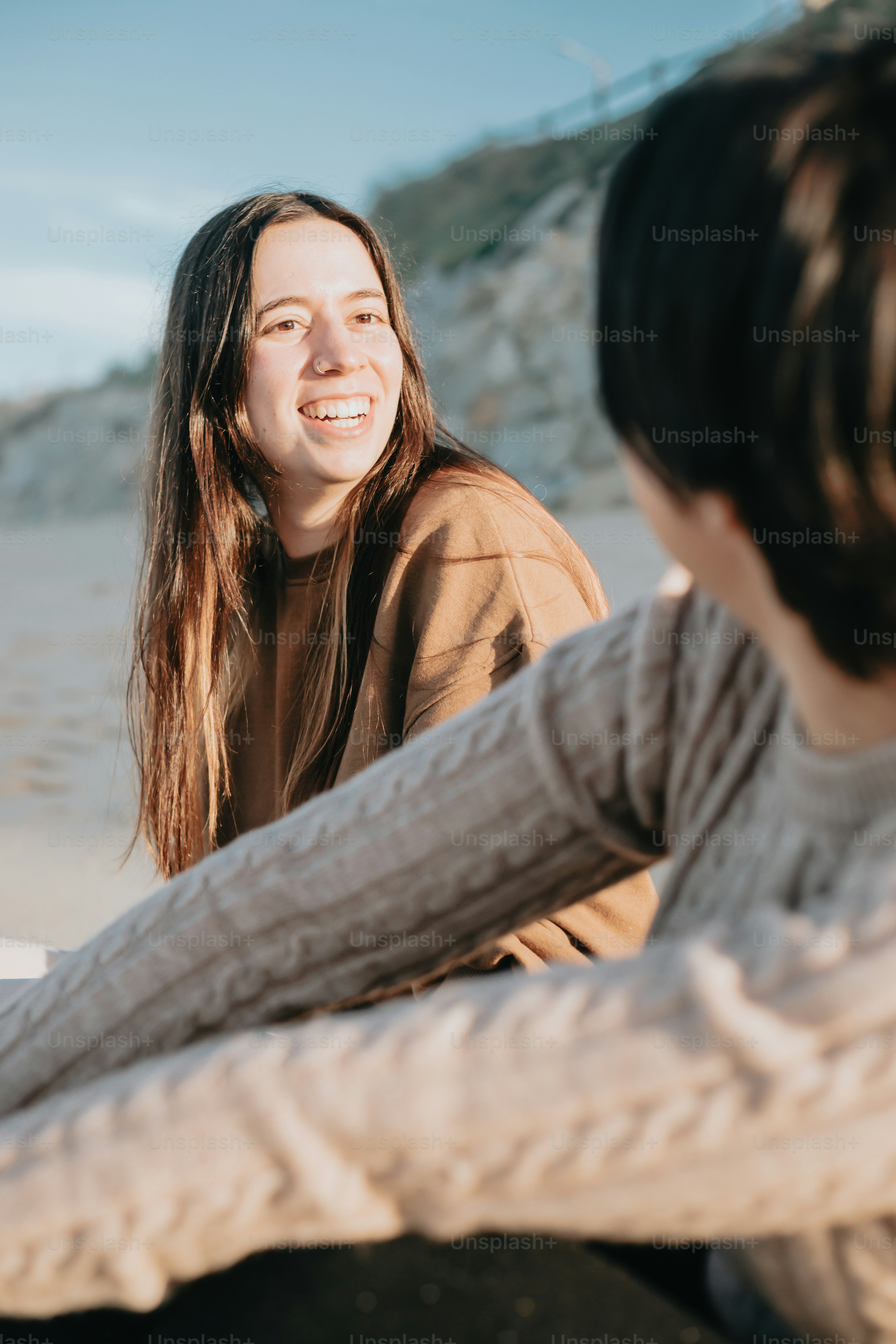 a woman sitting next to another woman on a beach