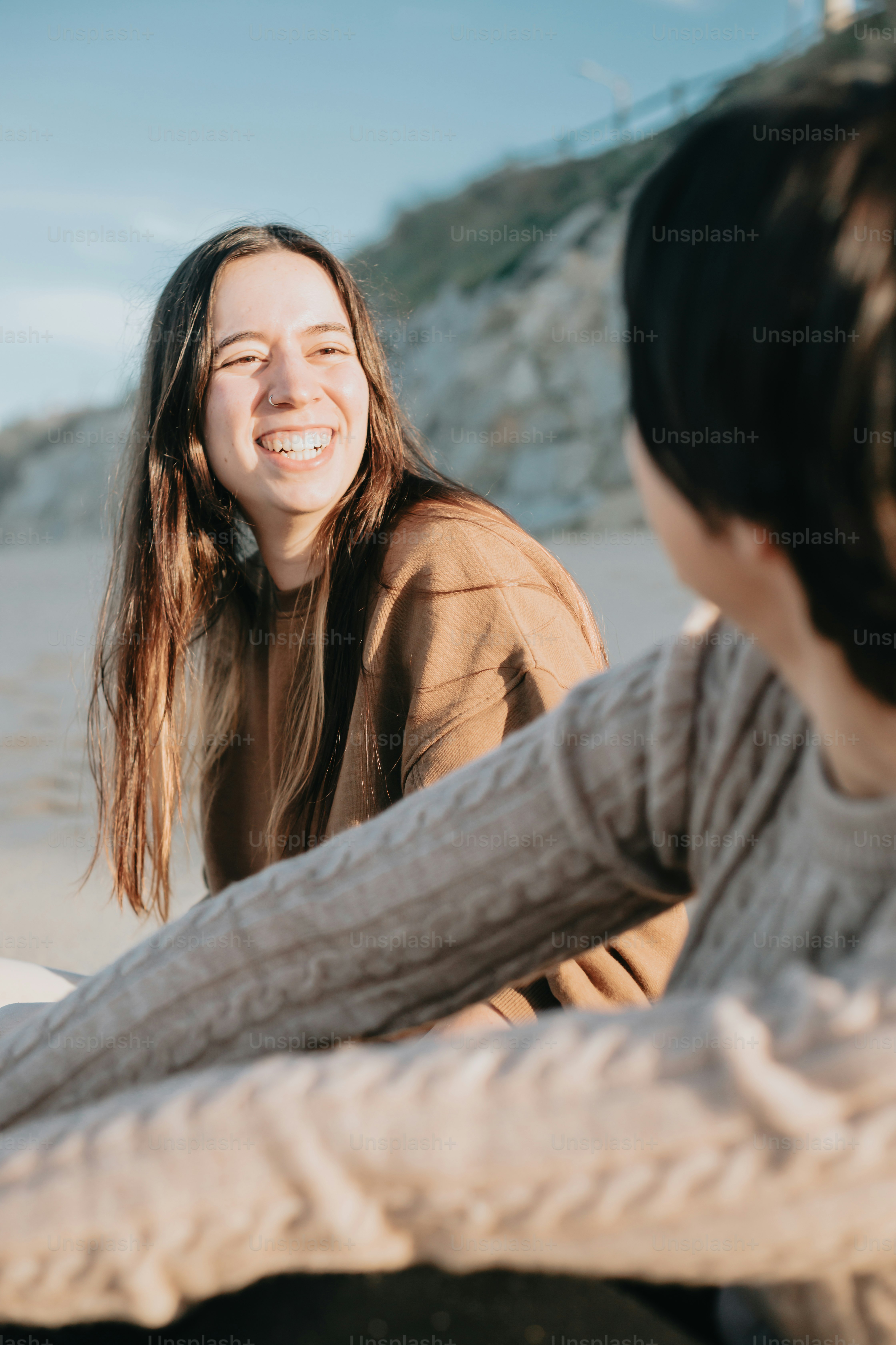 a woman sitting next to another woman on a beach