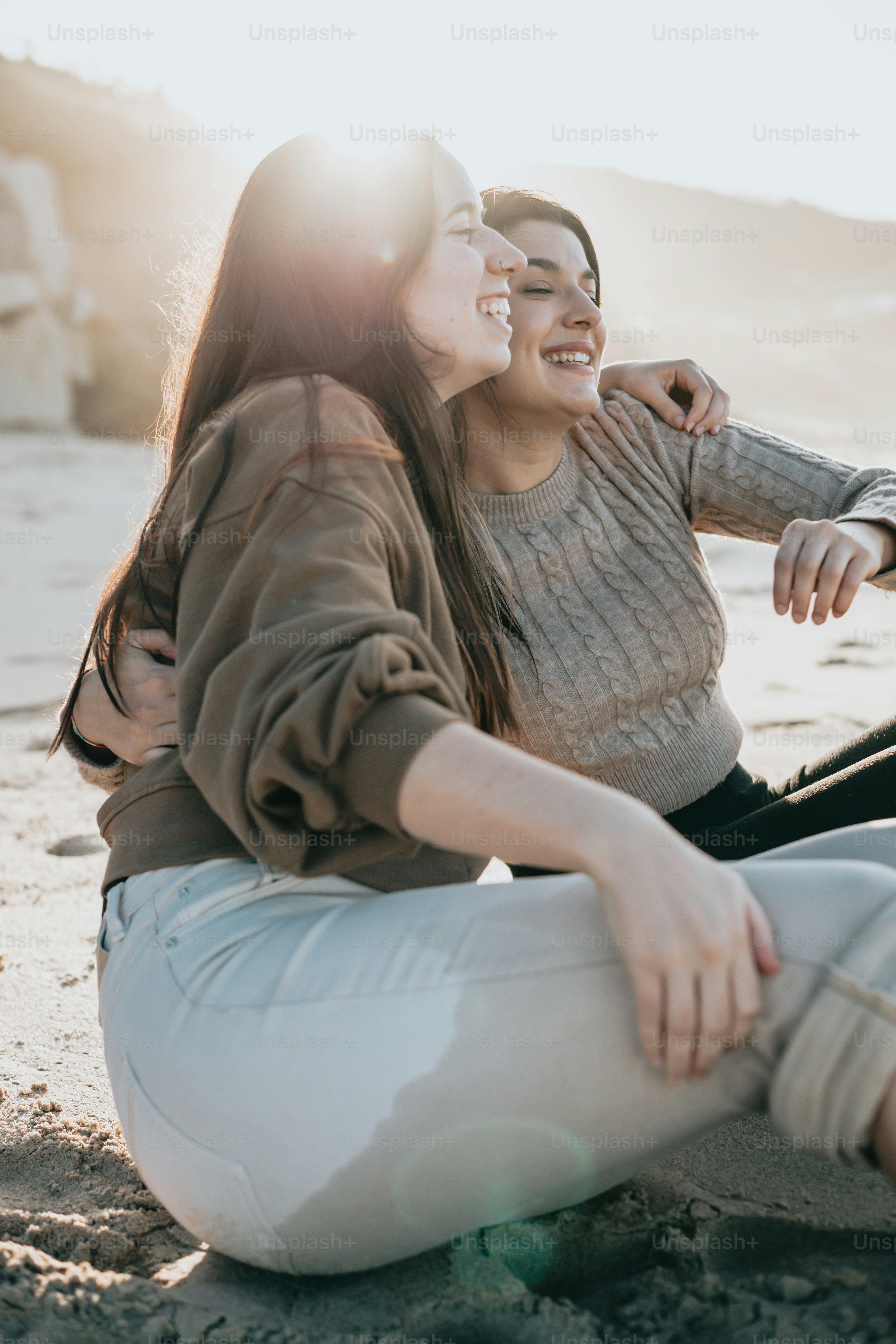 a couple of women sitting on top of a sandy beach