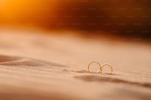 a pair of gold earrings sitting on top of a sandy beach