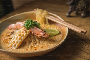a bowl of noodles and shrimp with chopsticks