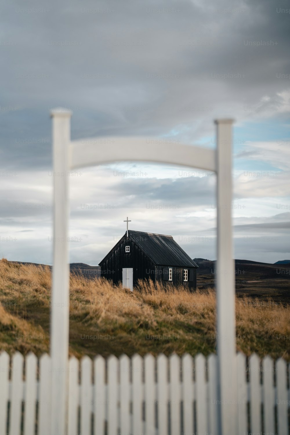 uma pequena casa preta em um campo com uma cerca branca