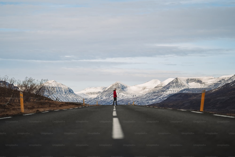 uma pessoa andando em uma estrada com montanhas nevadas ao fundo
