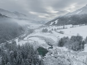 a snow covered valley with a river surrounded by trees