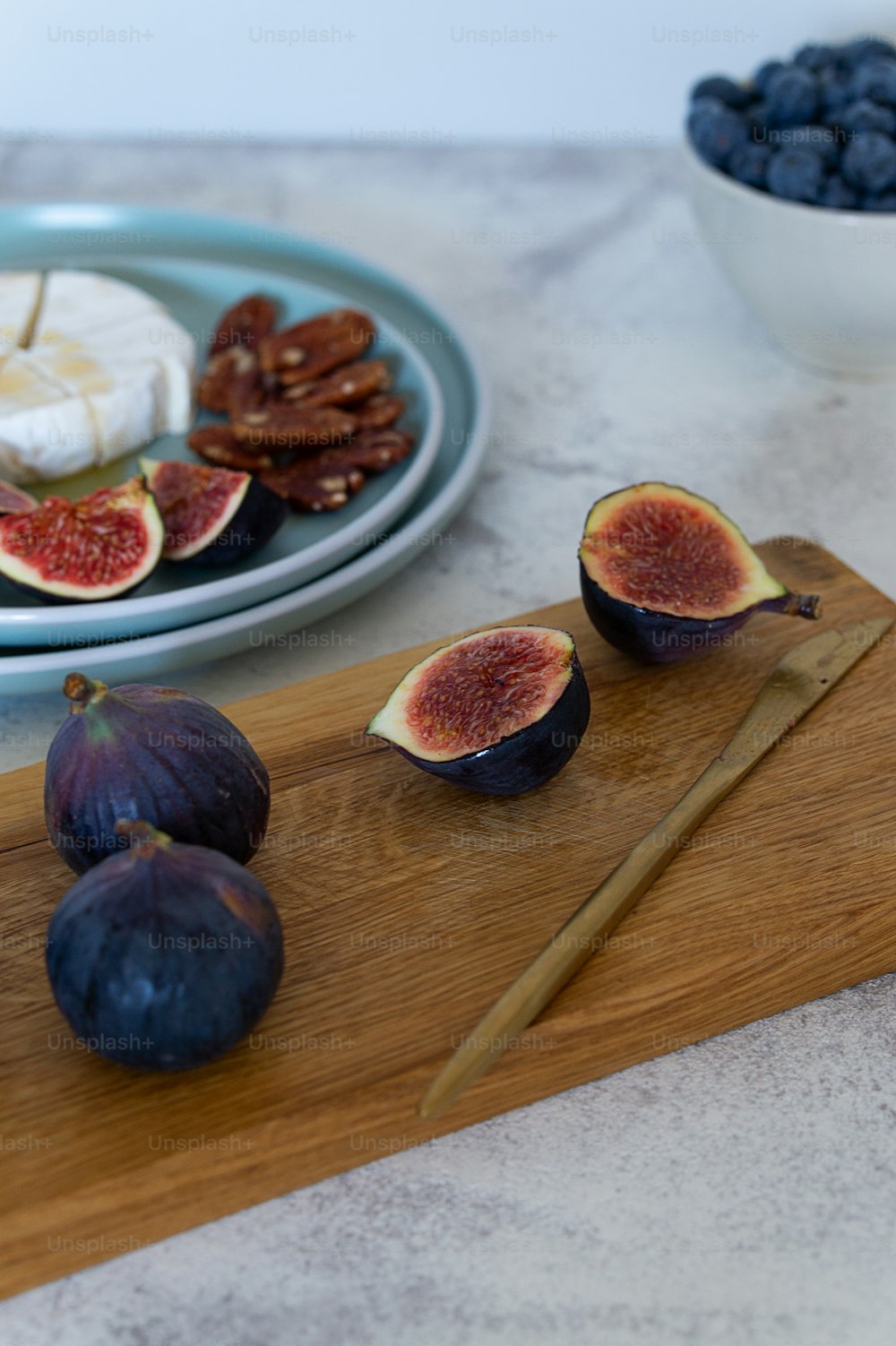 a wooden cutting board topped with figs next to a bowl of blueberries