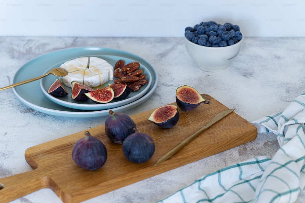 figues et fromage sur une planche à découper avec un bol de bleuets