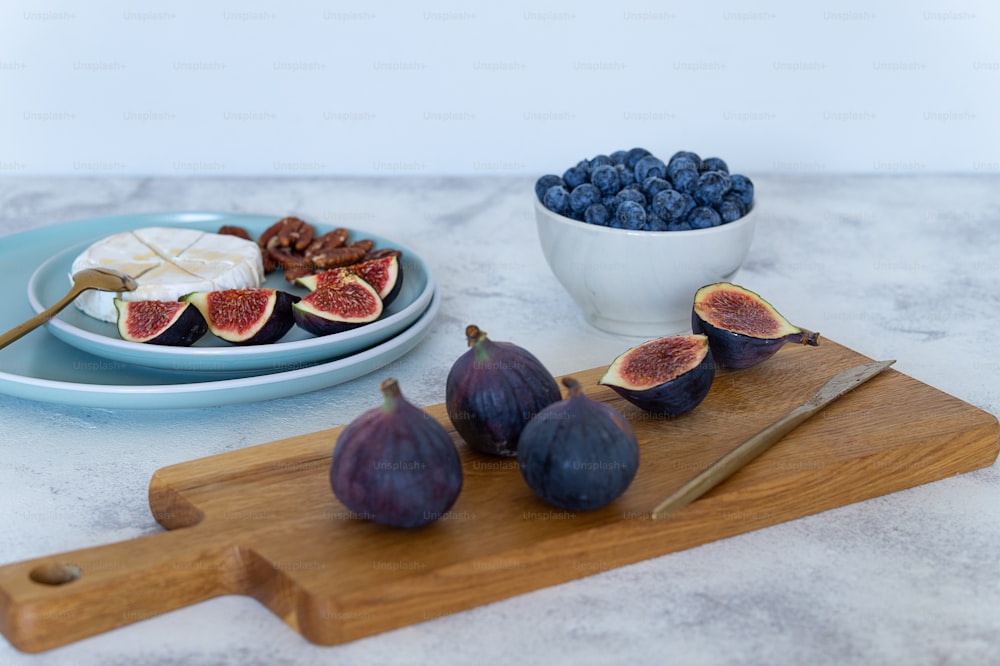 a cutting board topped with figs next to a bowl of blueberries