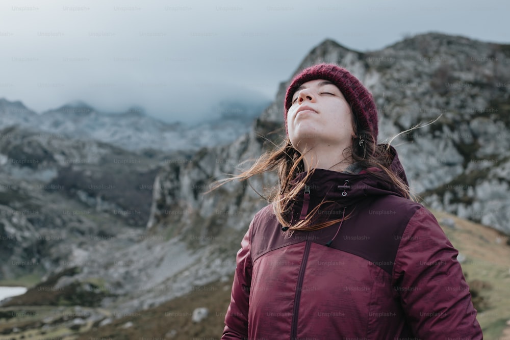 Una mujer parada en la cima de una montaña con los ojos cerrados