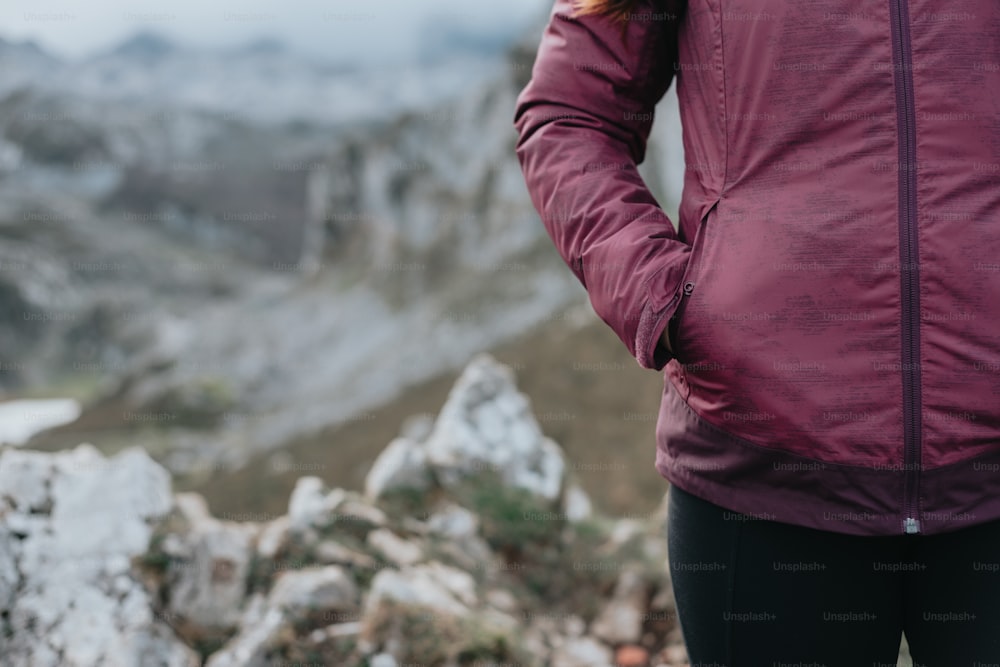 Una mujer parada en la cima de una montaña con las manos en los bolsillos