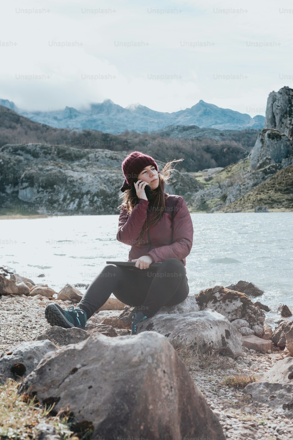 a woman sitting on a rock talking on a cell phone