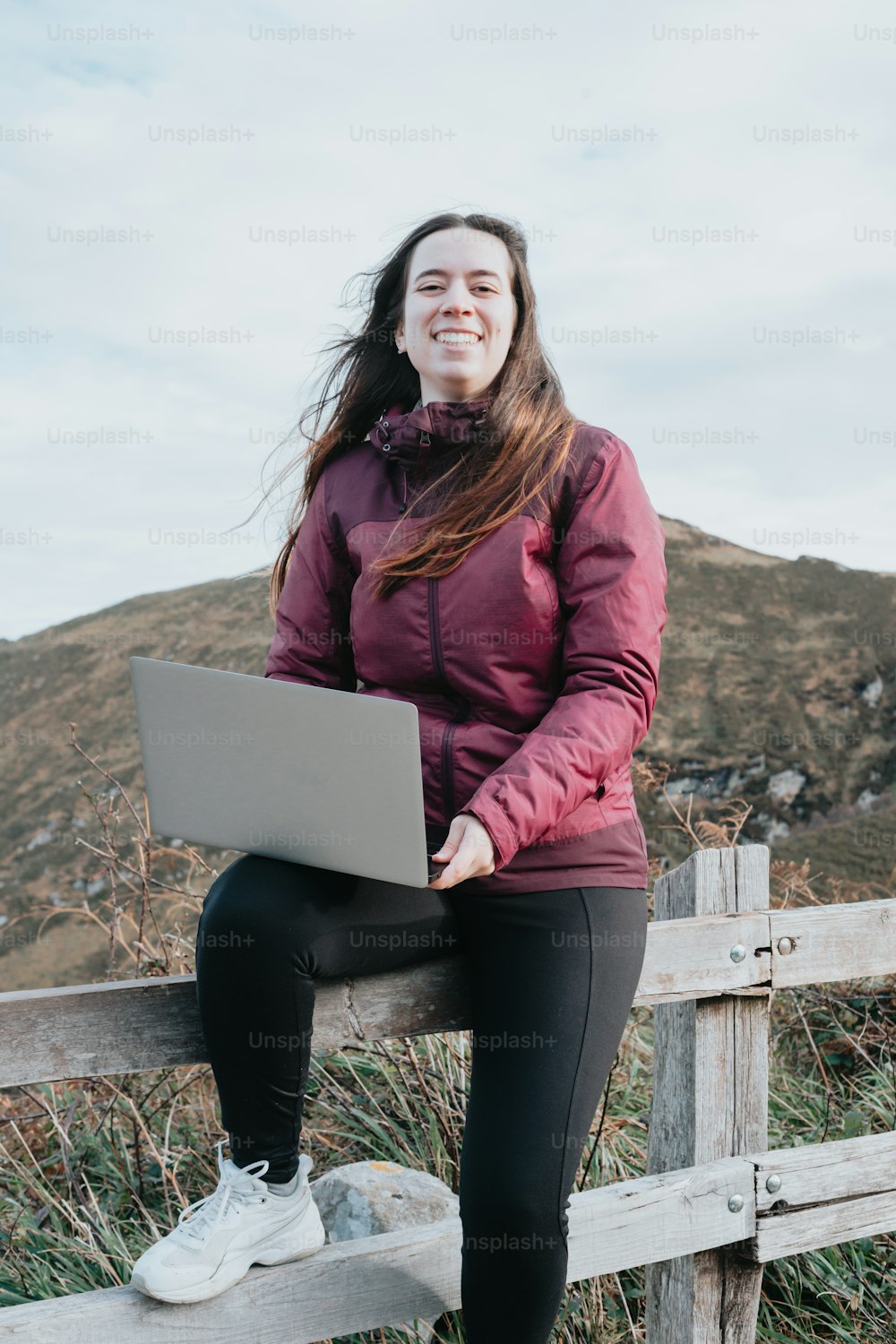 Una mujer sentada en una cerca con una computadora portátil
