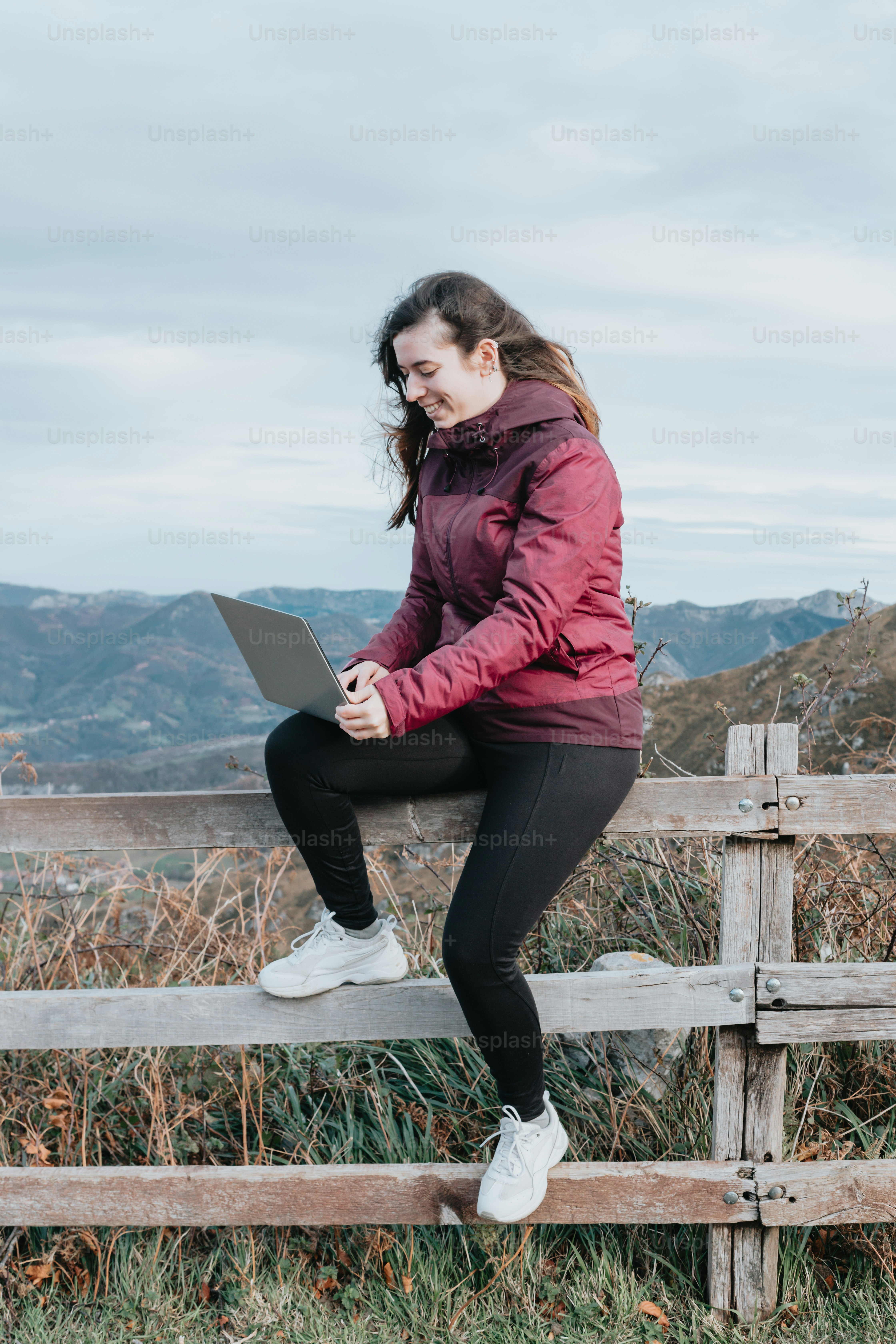 a woman sitting on a fence with a laptop