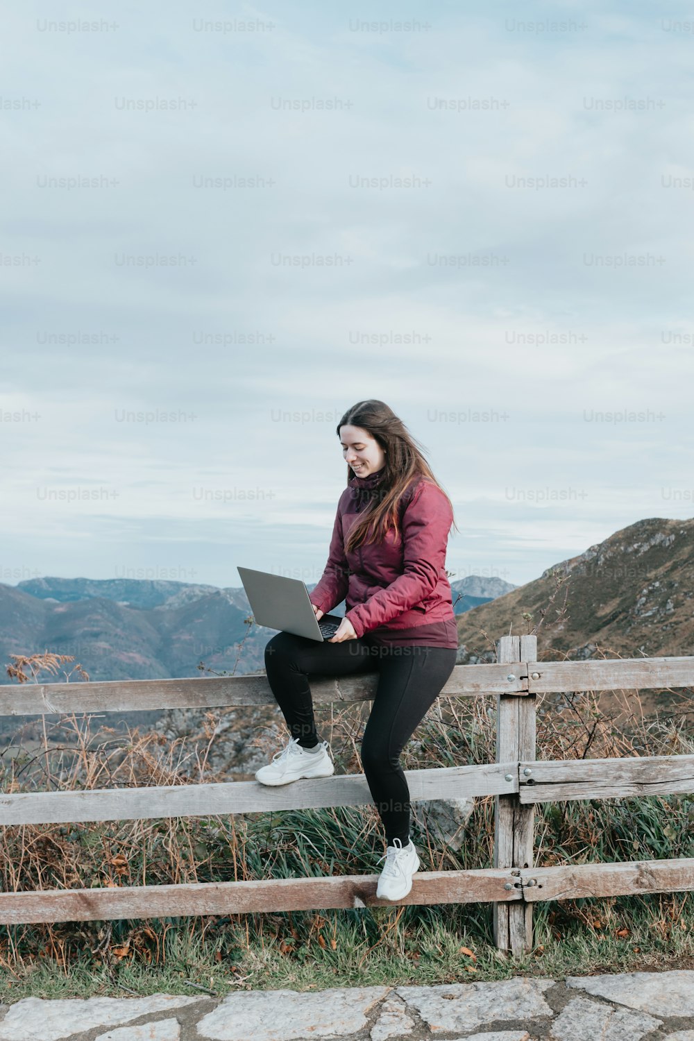 a woman sitting on a fence with a laptop