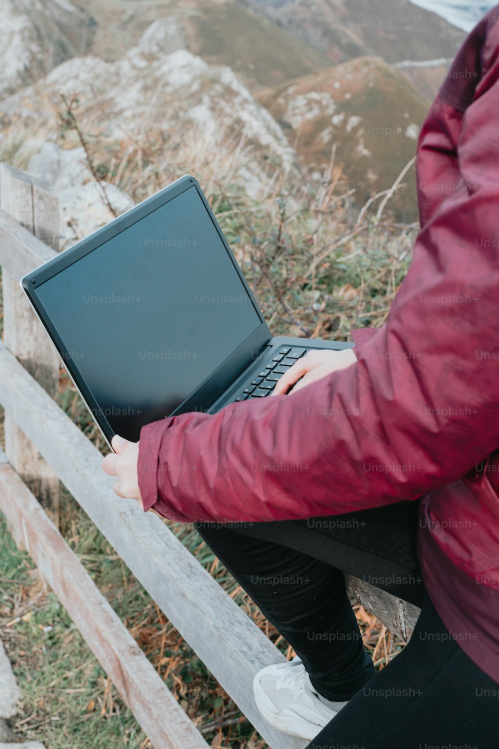 a woman sitting on a fence using a laptop computer