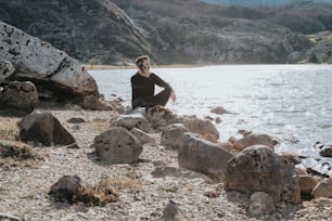 um homem sentado em uma rocha ao lado de um corpo de água