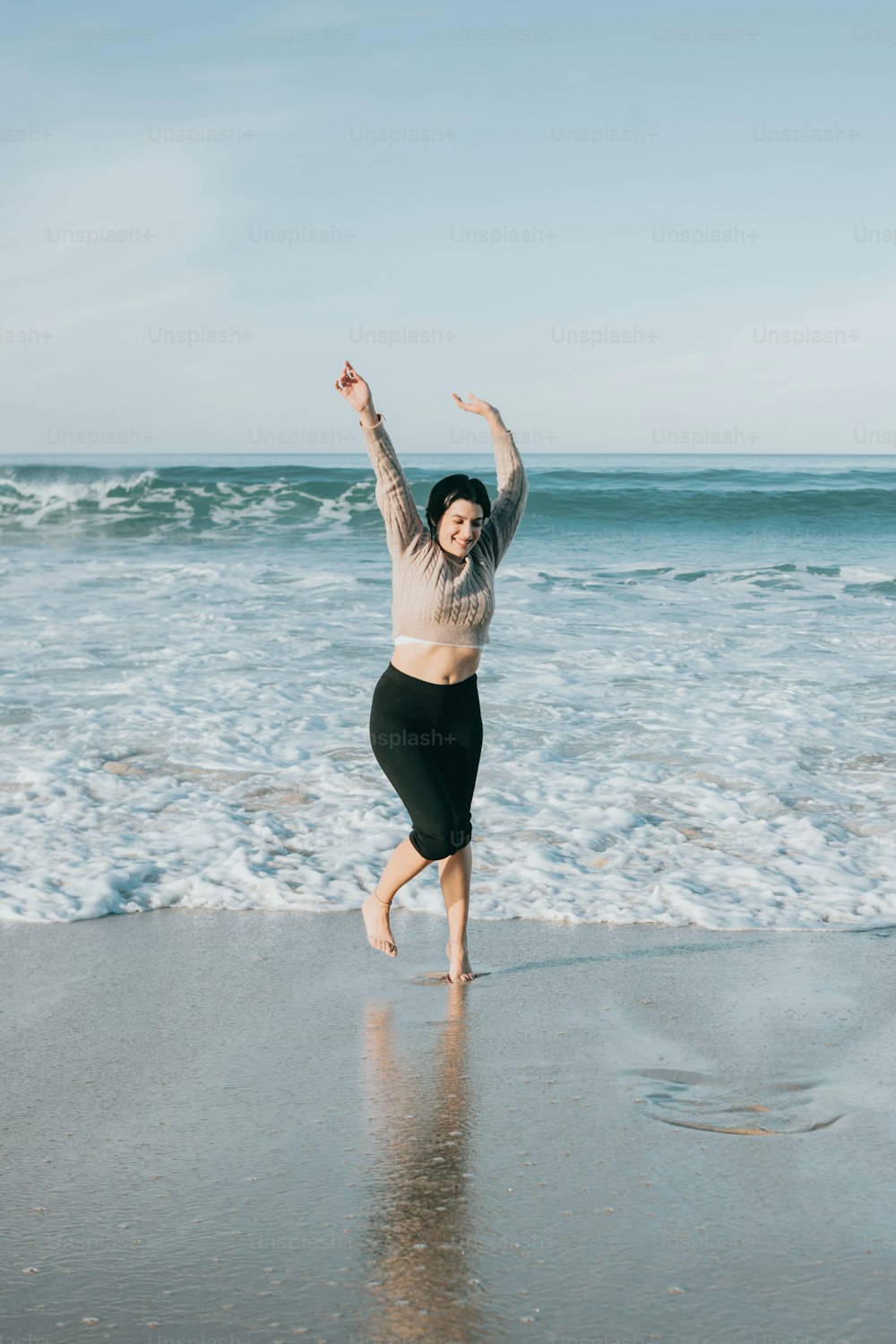 uma mulher pulando na praia em frente ao oceano