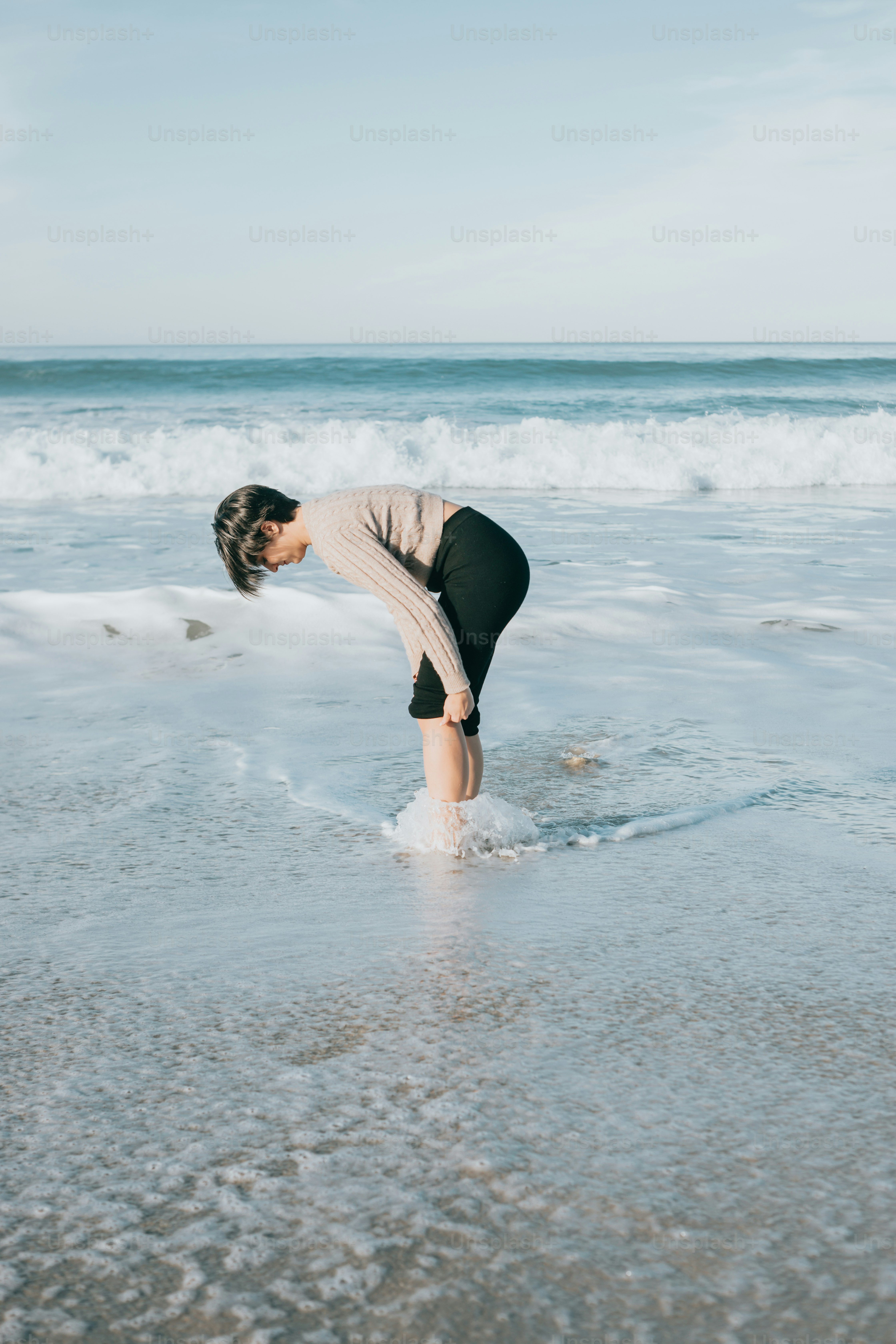 A woman standing on top of a sandy beach next to the ocean photo ...