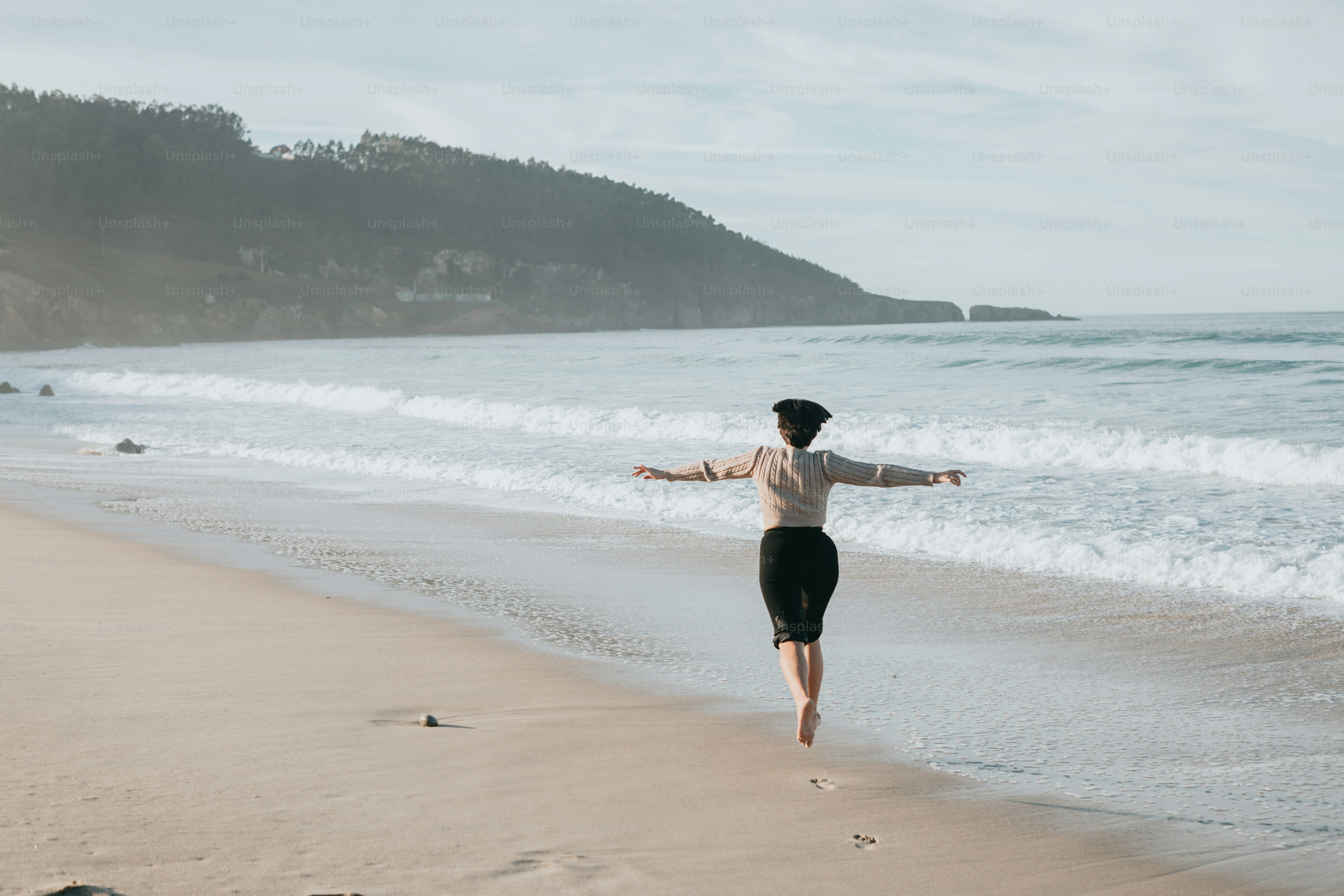 A woman standing on top of a sandy beach next to the ocean photo ...