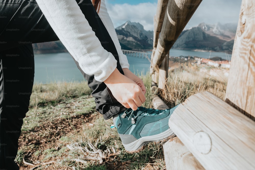 a person tying a shoe on top of a wooden bench