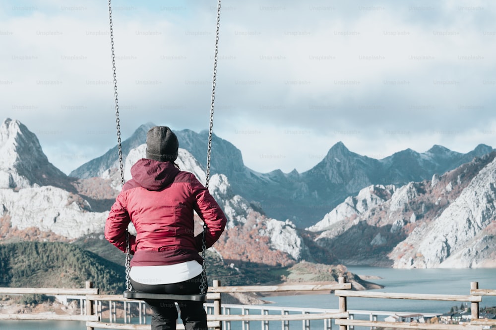 a woman sitting on a swing in front of mountains