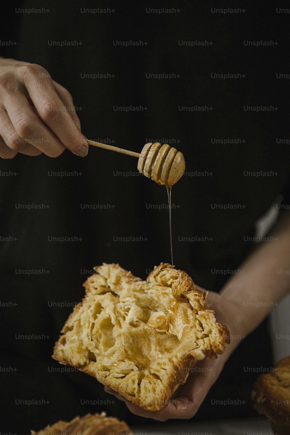 una persona sosteniendo un pedazo de pan y un palillo de miel