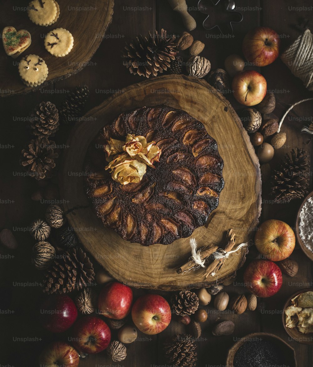 a wooden plate topped with a pastry next to apples and pine cones