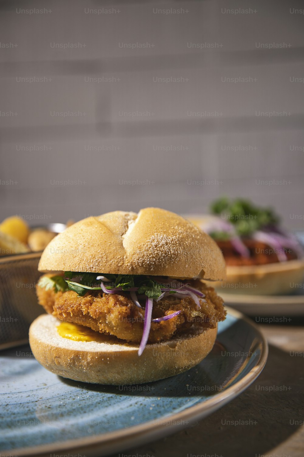 a chicken sandwich on a plate with a bowl of salad in the background
