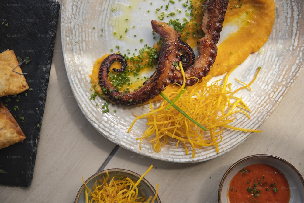 un plato blanco cubierto con comida junto a un tazón de salsa