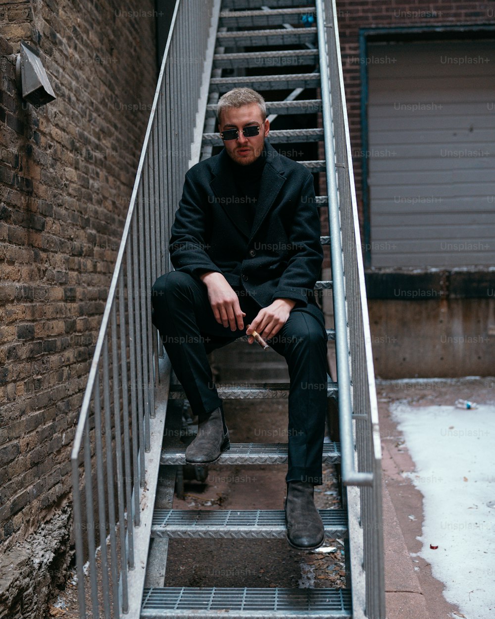 a man in a suit and sunglasses sitting on a set of stairs