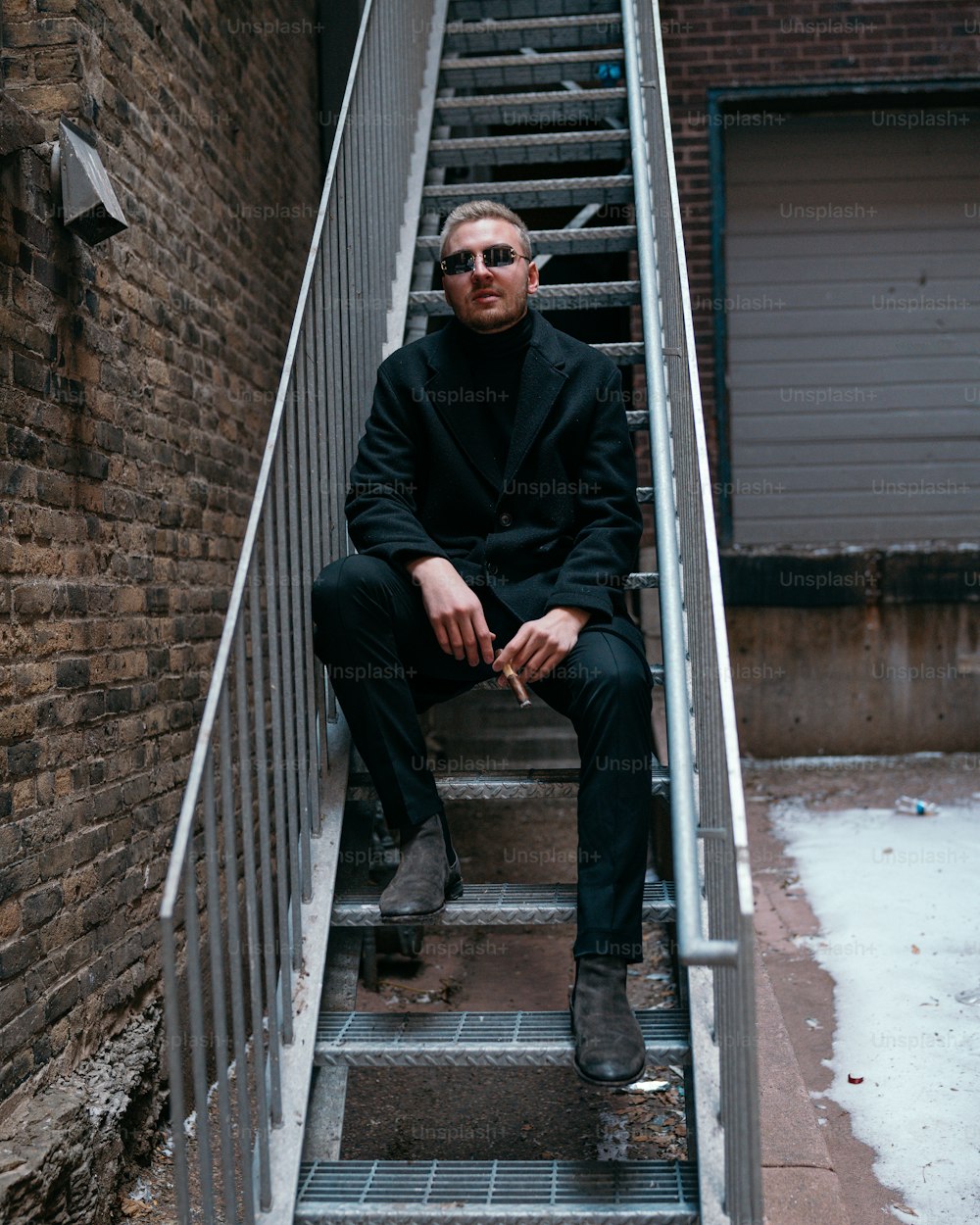 a man in a black suit sitting on a set of stairs