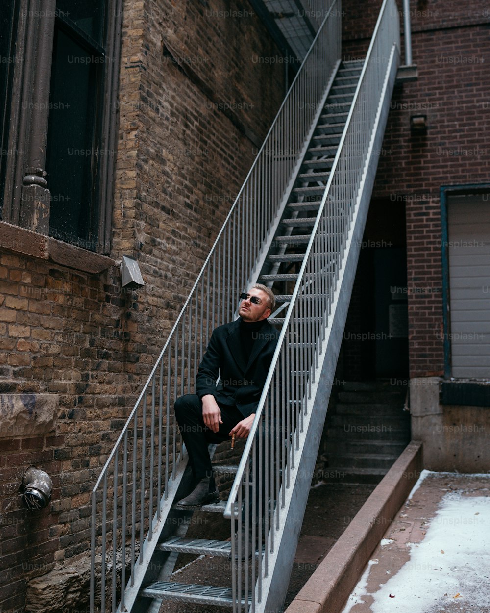 Un homme assis sur une cage d’escalier à côté d’un bâtiment en briques