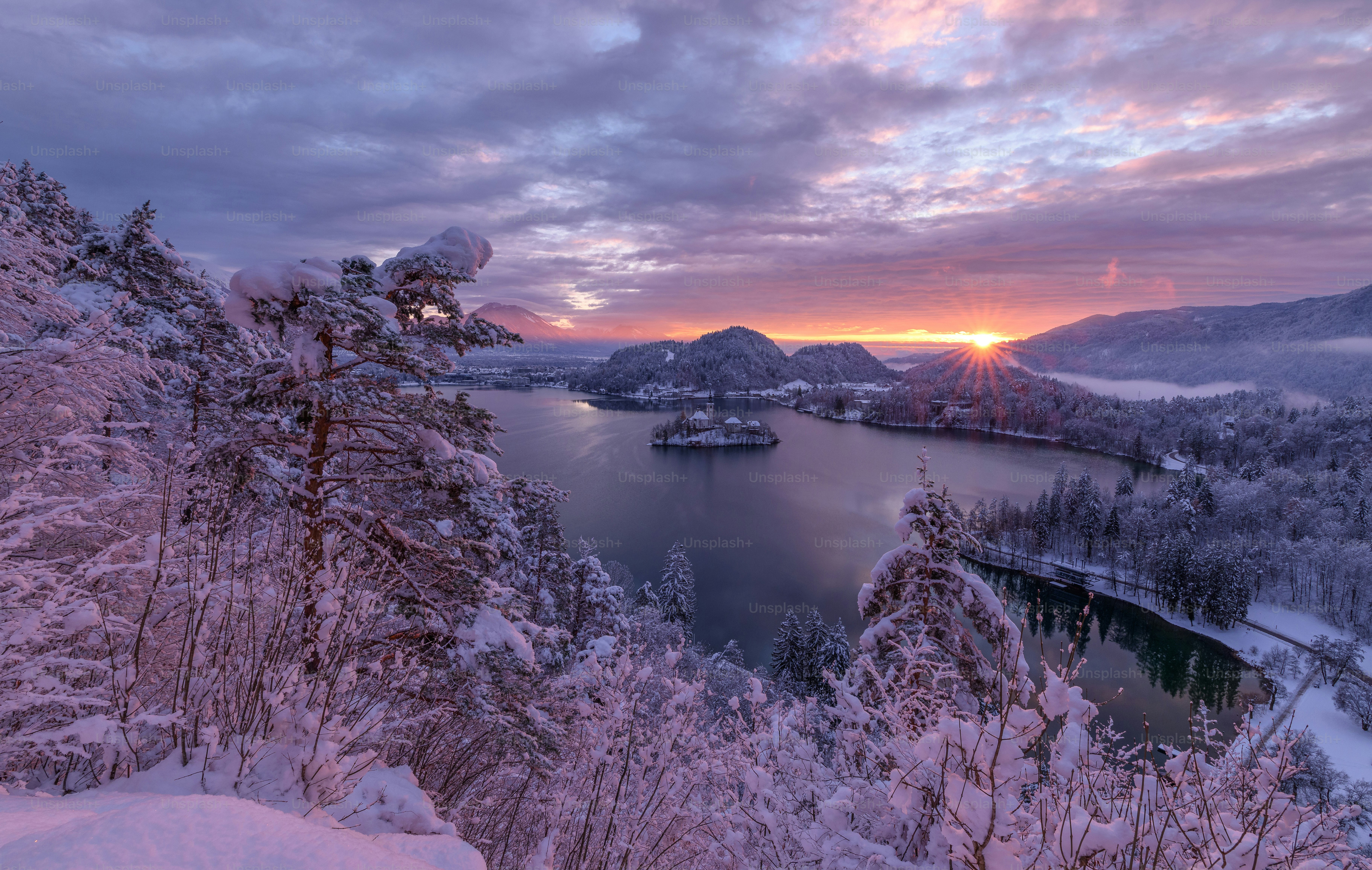 a lake surrounded by snow covered trees under a cloudy sky