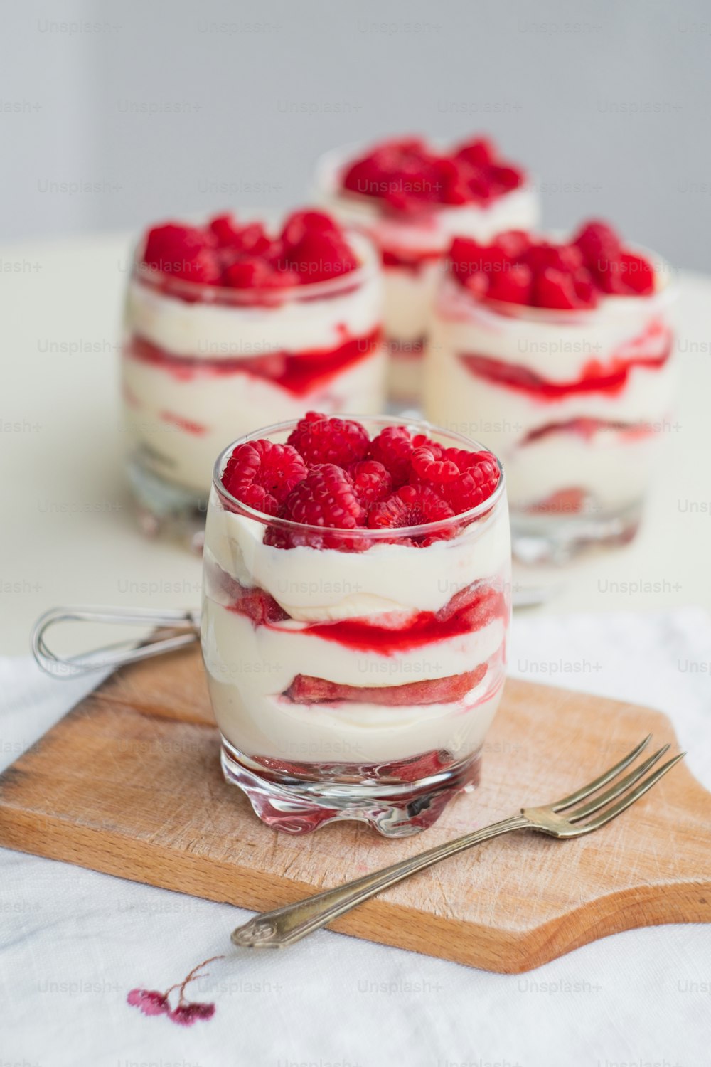 three desserts with raspberries in a glass on a cutting board
