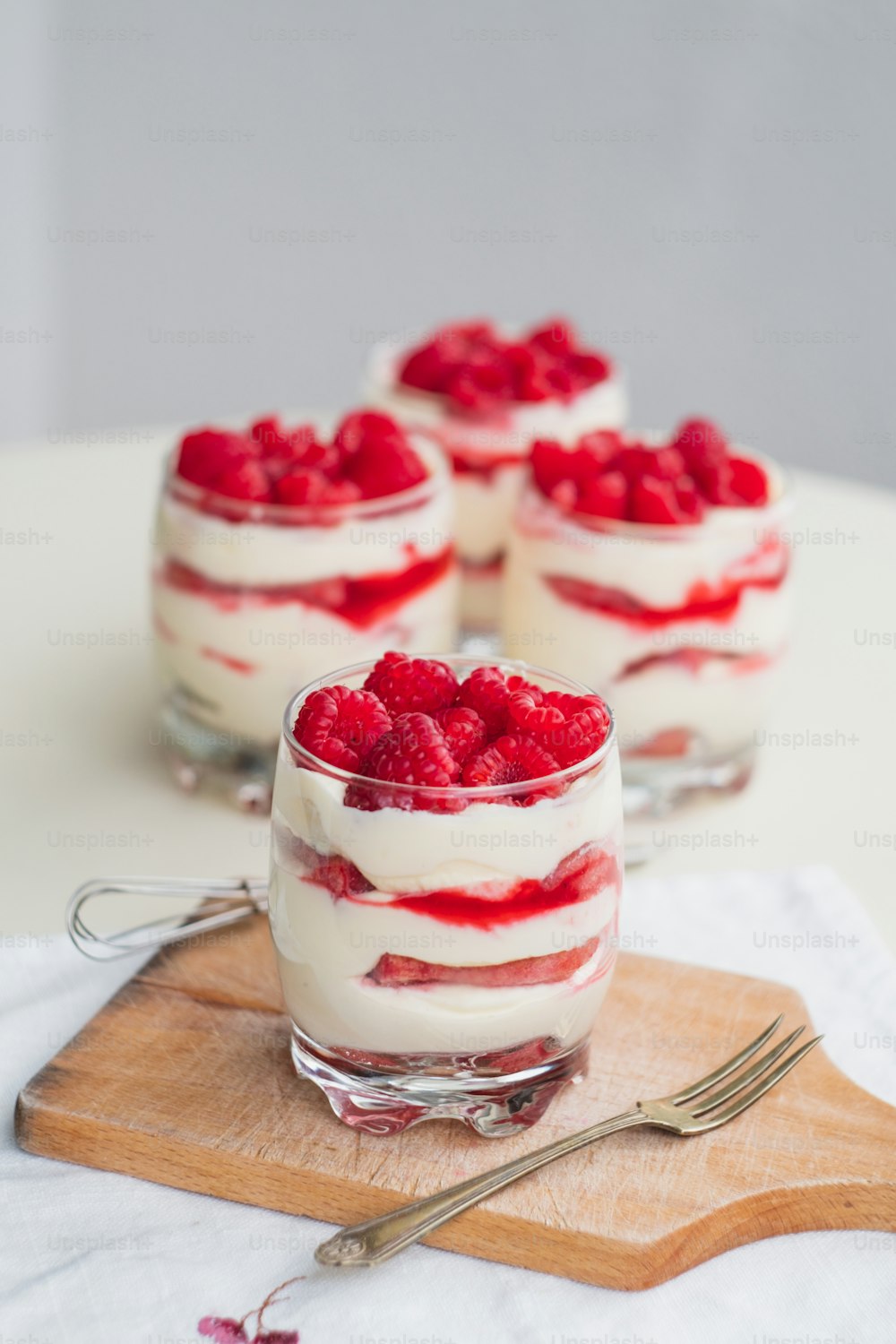 three small desserts with raspberries on top of a cutting board