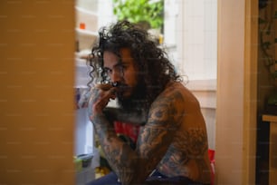 a man with long curly hair and tattoos smoking a cigarette