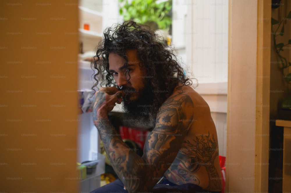 a man with long curly hair and tattoos smoking a cigarette