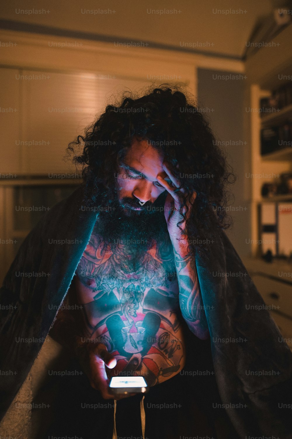 Un uomo con capelli lunghi e tatuaggi che tengono un telefono cellulare