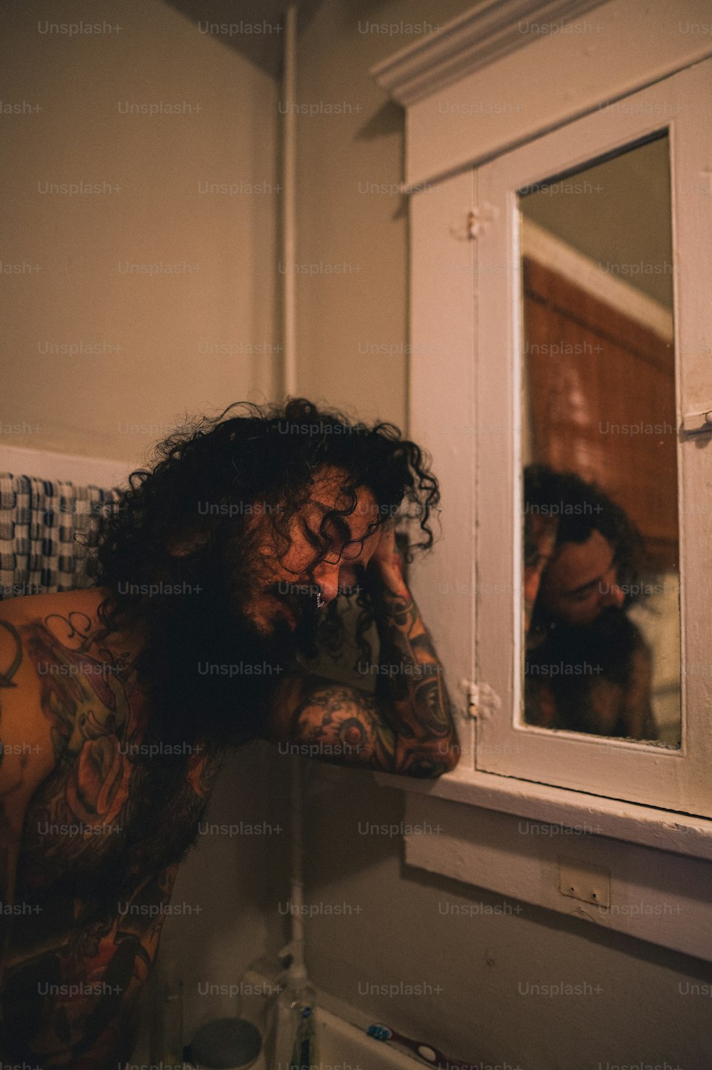 a man with long hair and tattoos looking in a mirror