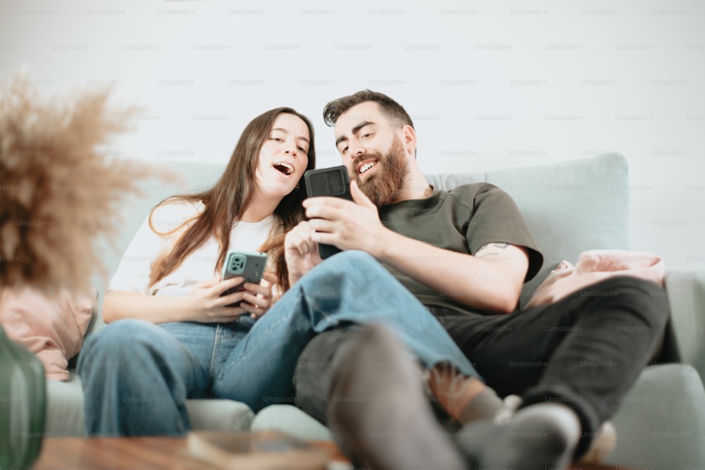 a man and woman sitting on a couch and looking at their phones