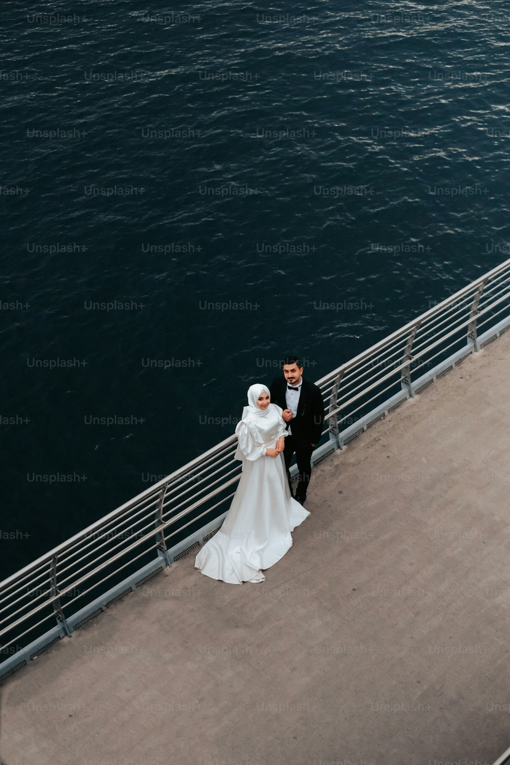 Una novia y un novio parados en un muelle junto al agua